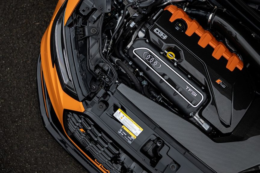 Motorhaube eines Autos mit sichtbarem Motor und orangefarbenen Akzenten.